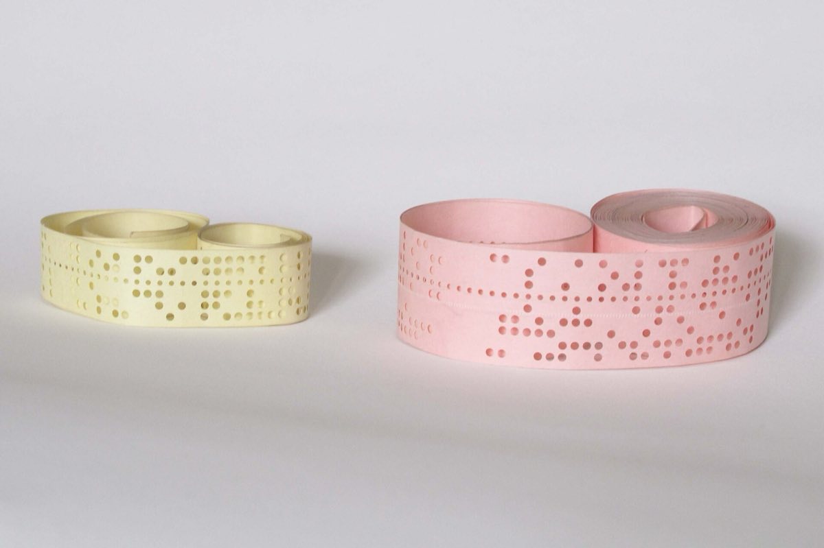 Two coils of punched paper tape, one 5-hole and one 8-hole, on a pale ground.